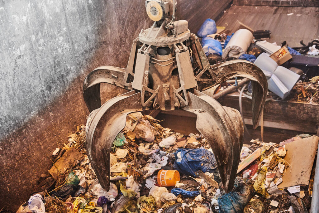 Ein Greifarm eines Krans schwebt über einer Mülldeponie.