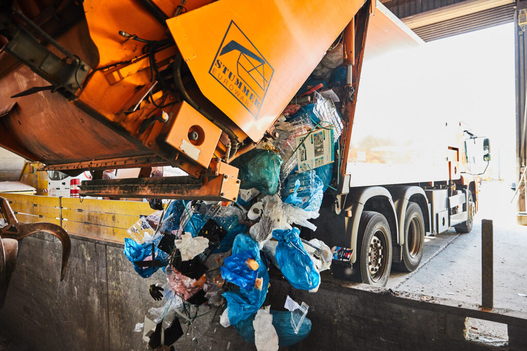 Ein oranger Müll-Lastwagen entleert Abfälle in einen Container.